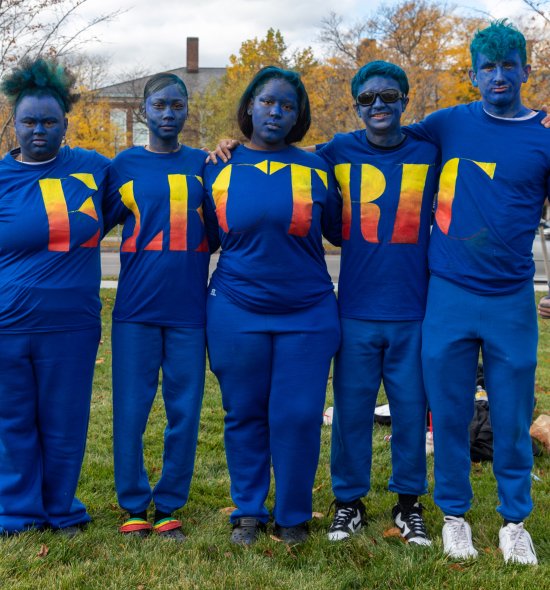 A group of teenagers in blue facepaint and blue clothing spelling out "Electric" in orange and yellow font